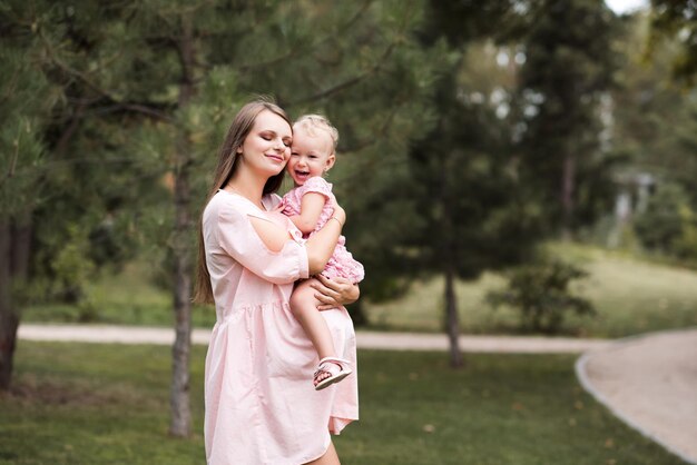 Femme enceinte tenant bébé fille posant avec les yeux fermés sur fond de nature dans le parc à l'extérieur Maternité Maternité