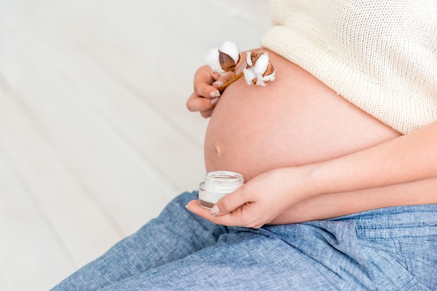 Femme enceinte tenant une branche de crème et de coton près de son ventre