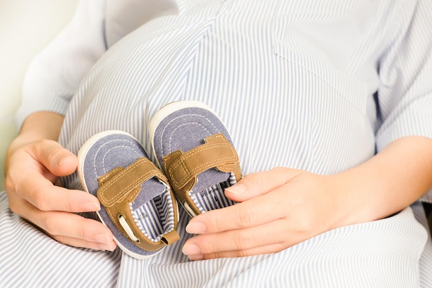 Femme enceinte tenant des chaussures de bébé dans les mains Soins prénataux de maternité et concept de grossesse de femme