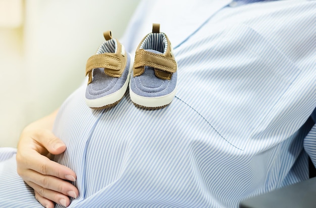 Femme enceinte tenant des chaussures de bébé dans ses mains Soins prénataux de maternité et concept de grossesse de femme