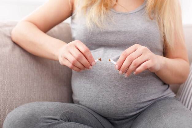 Femme enceinte tenant une cigarette cassée près du ventre. Des soins d'attente méconnaissables pour son futur bébé. Mode de vie sain, mauvaises habitudes, soins de santé, concept de dépendance