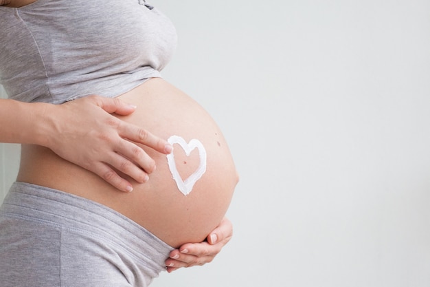 Femme enceinte tenant coeur rouge et la main sur son ventre, symbole d'une nouvelle vie, concept d'attendre pour bébé et élargir la famille