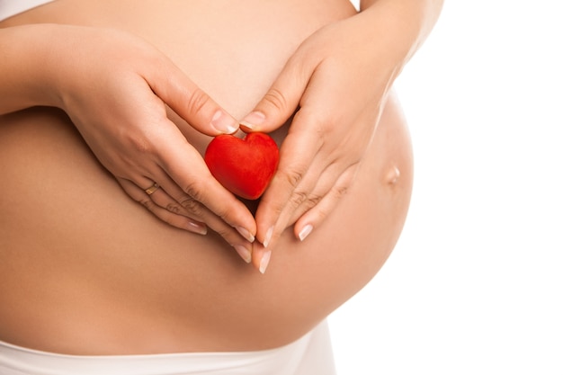 Femme enceinte tenant dans ses mains le symbole du coeur sur blanc