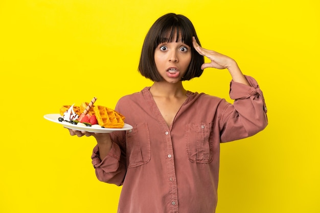 Femme enceinte tenant des gaufres isolées sur fond jaune avec une expression surprise