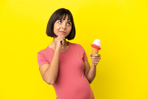 Femme enceinte tenant une glace au cornet isolée sur fond jaune et levant