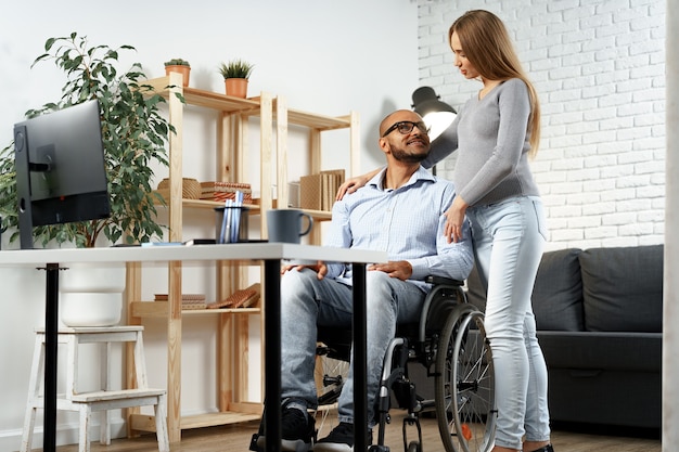 Femme enceinte tenant une main de son mari handicapé assis dans un fauteuil roulant