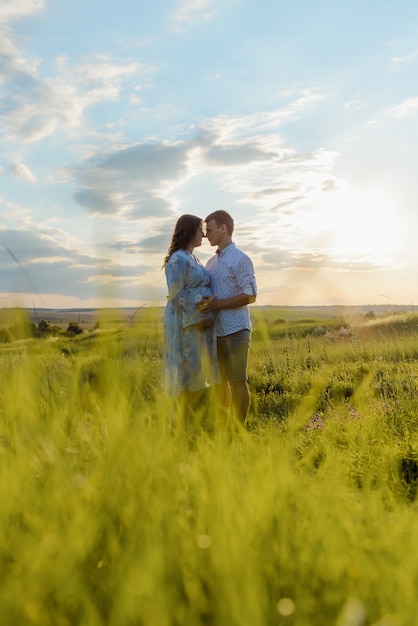 Femme enceinte tenant la main avec son mari lors d'une promenade sur le terrain au coucher du soleil. Héhé et nouveau-né.