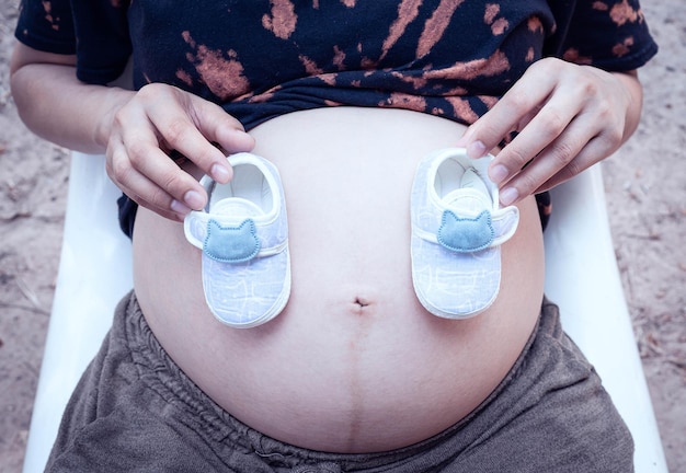 Photo femme enceinte tenant une paire de chaussures de bébé