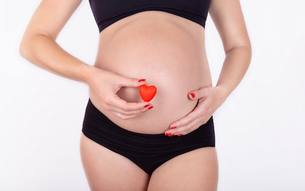Une femme enceinte tenant un petit coeur rouge dans sa main