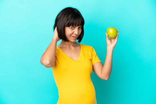 Femme enceinte tenant une pomme isolée sur fond bleu ayant des doutes