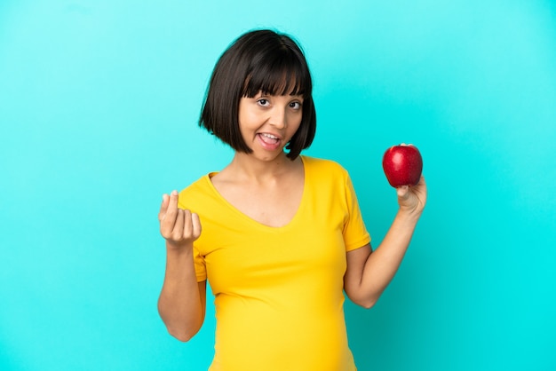 Femme enceinte tenant une pomme isolée sur fond bleu faisant un geste d'argent