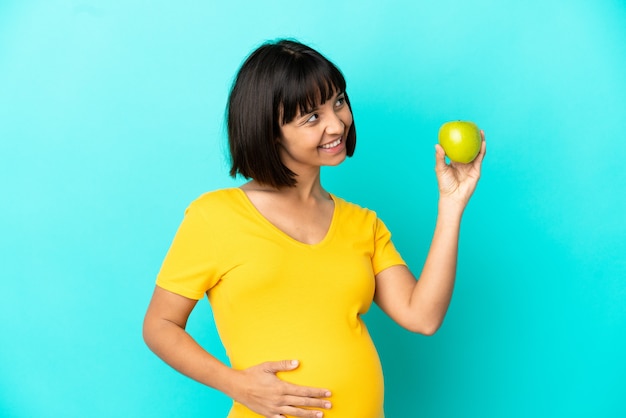 Femme enceinte tenant une pomme isolée sur fond bleu en pensant à une idée tout en levant les yeux