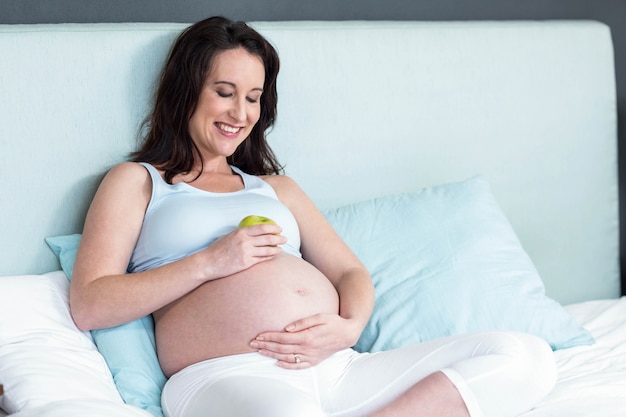 Femme enceinte tenant une pomme sur le ventre à la maison