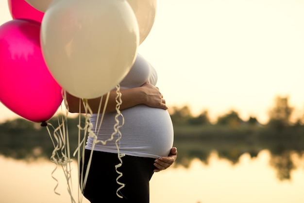 Femme enceinte tenant son ventre et ballons sur un coucher de soleil