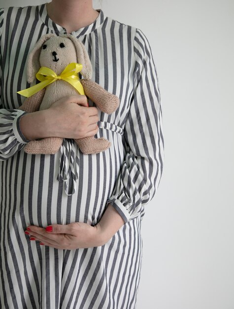 Une femme enceinte tenant son ventre et un ours en peluche lapin