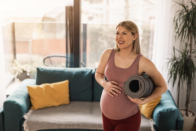 Une femme enceinte tenant un tapis d'exercice est prête à pratiquer le yoga à la maison le matin.