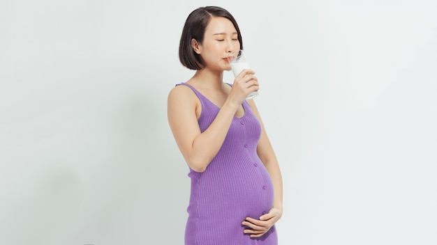 femme enceinte tenant un verre de lait frais et touchant son ventre avec les mains sur fond blanc