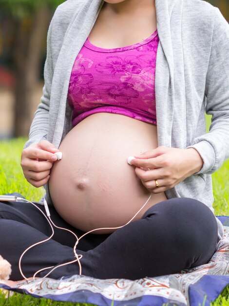 Femme enceinte, tenue, écouteurs, sur, elle, ventre, dans, jardin