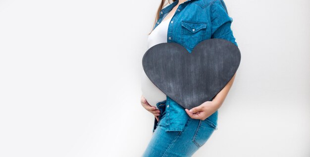 Une femme enceinte tient un coeur noir. Concept de grossesse, parentalité, préparation et attente. Fermer