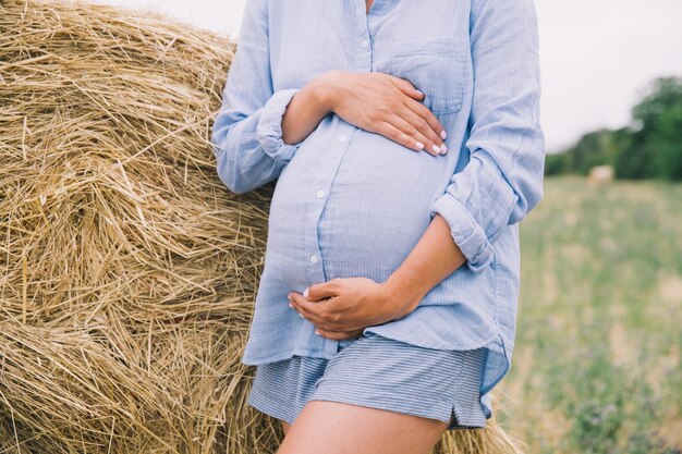 Une femme enceinte tient les mains sur le ventre sur le fond de la nature à l'extérieur