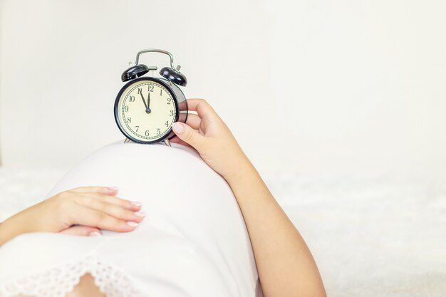 La femme enceinte tient un réveil dans les mains.