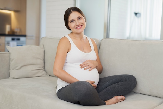 femme enceinte tient ses mains sur son ventre et sourit.