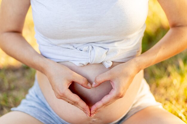 Photo une femme enceinte tient ses mains sur son ventre sous la forme d'un cœur