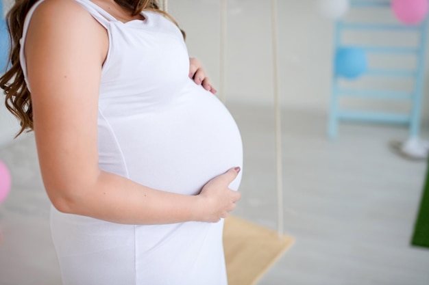 Une femme enceinte tient son ventre avec ses mains dans une robe blanche