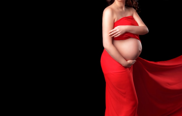 Femme enceinte en tissu mousseline rouge tient les mains sur le ventre dans l&#39;obscurité.