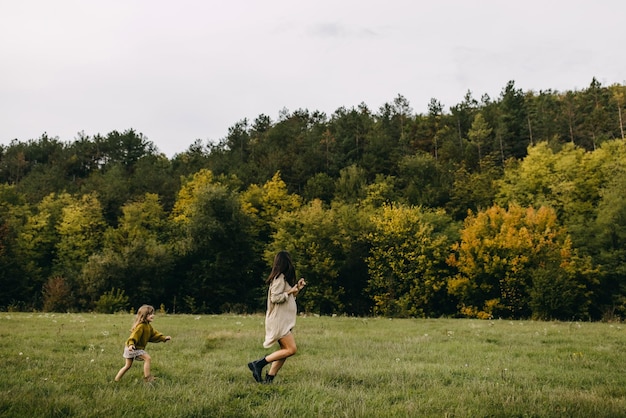 Une femme enceinte et un tout-petit à l'extérieur courent dans un champ avec de l'herbe verte et passent du temps ensemble