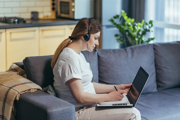 Femme enceinte travaillant à distance à la maison à l'aide d'un consultant de casque d'appel vidéo assis sur un canapé et travaillant avec un ordinateur portable à la maison