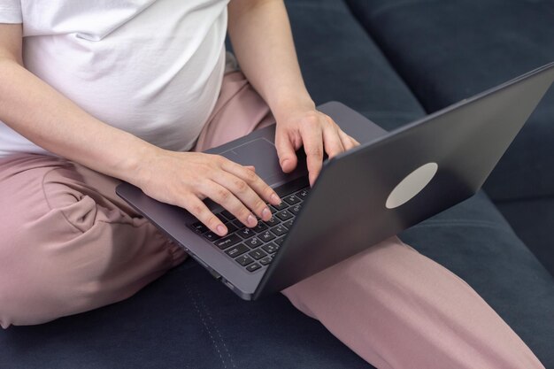 Femme enceinte travaillant sur un ordinateur portable assis sur un canapé à la maison