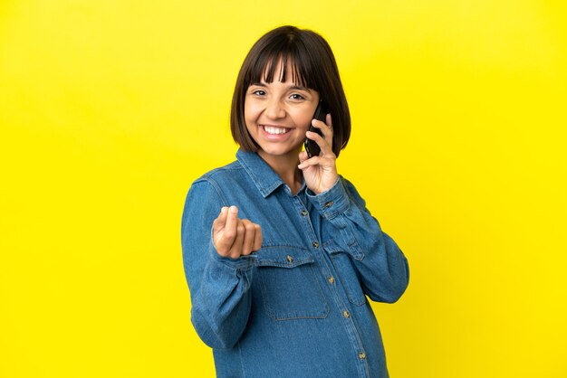 Femme enceinte utilisant un téléphone portable isolé sur fond jaune faisant un geste d'argent