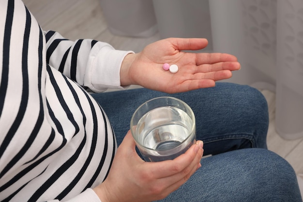 Femme enceinte avec un verre d'eau et une pilule à la maison en gros plan