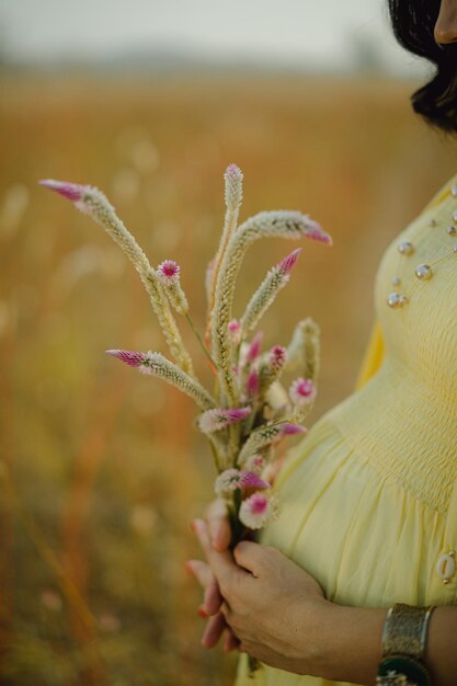 Femme enceinte, vêtue d'une robe jaune clair, tenant dans les mains un bouquet de fleurs de marguerite.