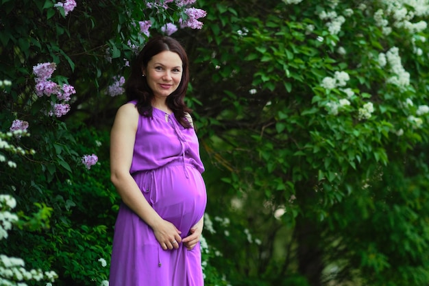 Une femme enceinte vêtue d'une robe violette se tient dans un jardin.