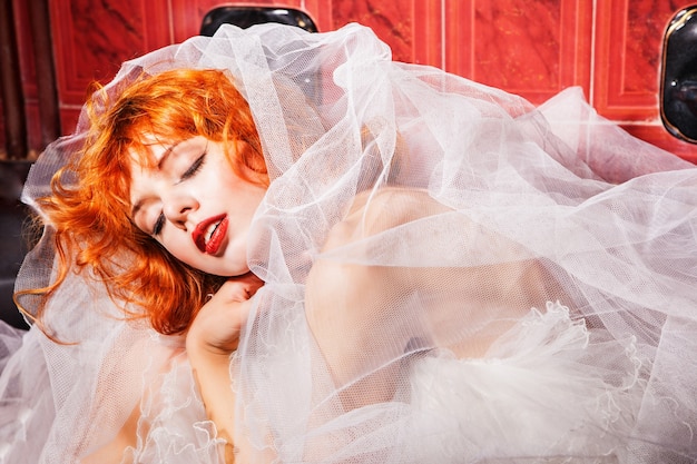 Femme endormie aux cheveux rouges en robe de mariée blanche dans la salle de bain