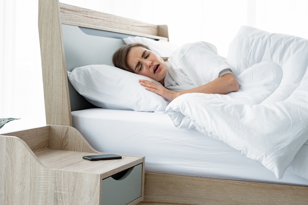 Femme endormie sur le lit et réveillée par l'horloge du téléphone.