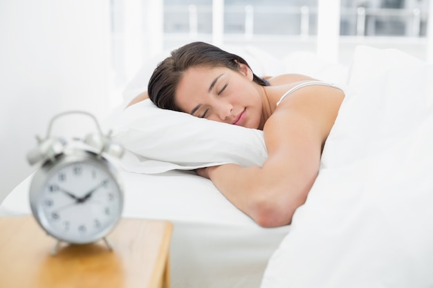 Femme endormie avec réveil flou sur la table de chevet