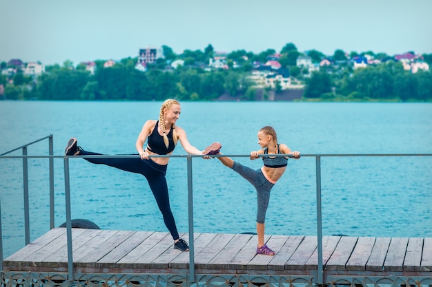 Femme et enfant font des exercices sportifs en étirant leurs jambes sur la jetée du lac