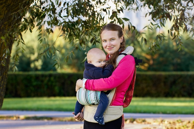 Femme avec enfant en porte-bébé se promène à l'extérieur au jour d'été