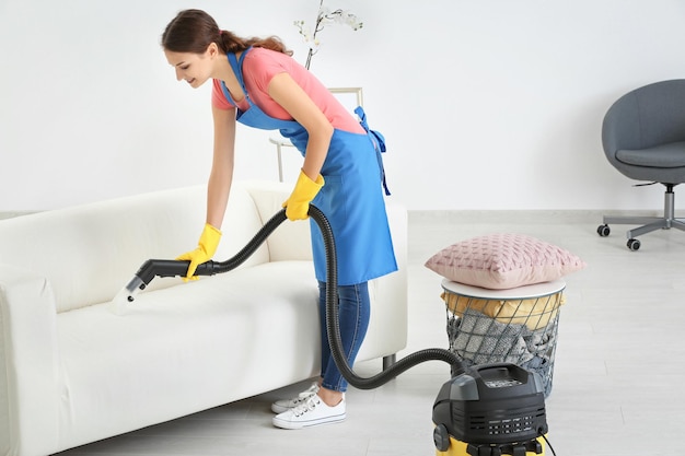 Femme enlevant la saleté du canapé à l'aide d'un aspirateur