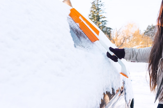 La femme enlève la neige de la voiture