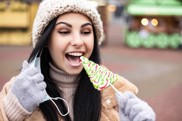 Une femme enlève son masque facial et mange des bonbons en se tenant à la foire des vacances d'hiver