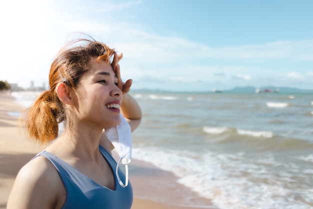 Une femme enlève son masque et se repose après avoir fini de courir au bord de la plage en été