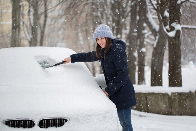 Femme enlever la neige du pare-brise de voiture