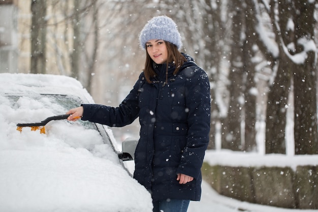 Femme enlever la neige du pare-brise de voiture