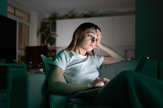 Une femme ennuyée allongée sur un canapé à l'aide d'un ordinateur portable tard dans la nuit à la maison ne peut pas dormir l'insomnie