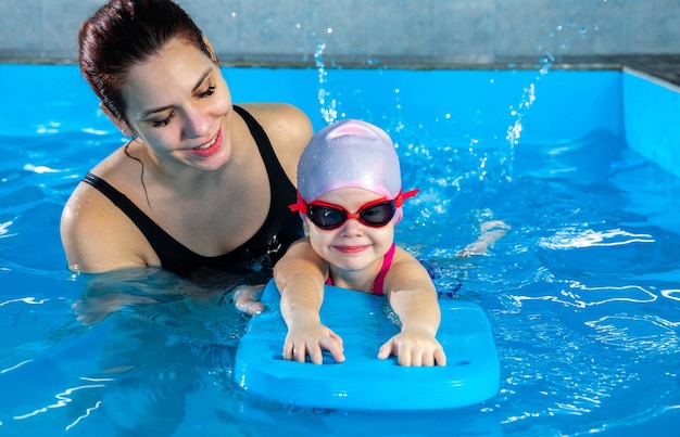 Femme enseignant à une petite fille comment nager dans une piscine intérieure avec planche flottante de piscine
