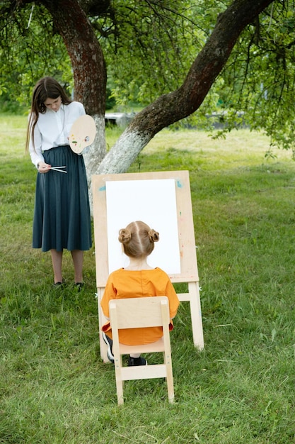 Une femme enseigne à un enfant à peindre dans le jardin